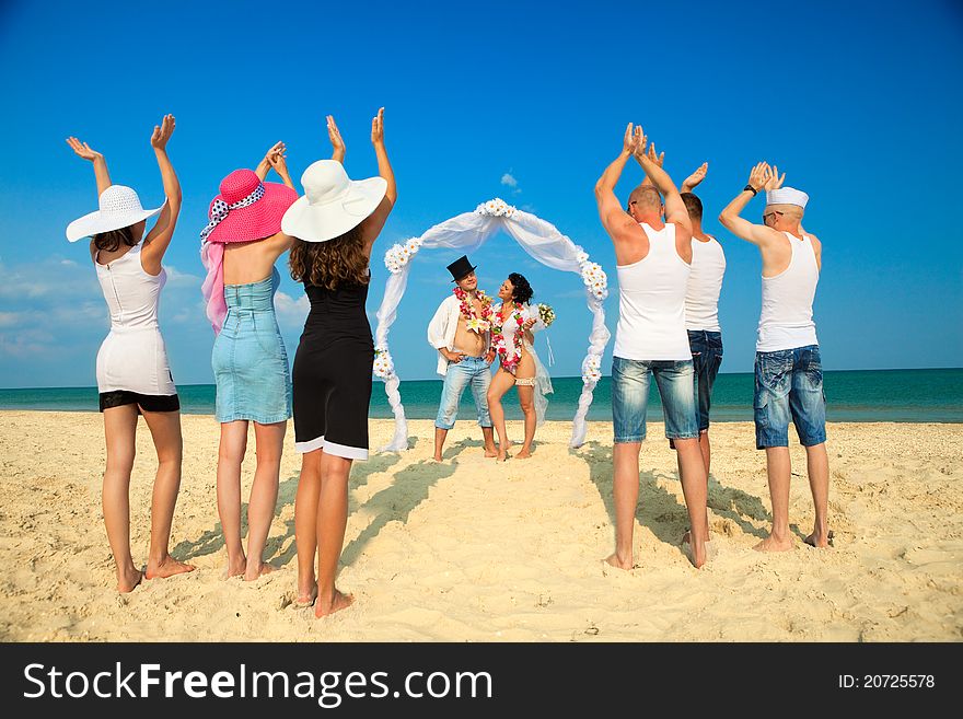 Groom with bride wearing lei, standing under archway on beach and their friends applauding for joy. Groom with bride wearing lei, standing under archway on beach and their friends applauding for joy