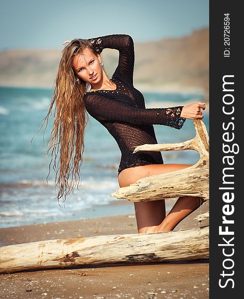 Young beautiful woman sitting on the log on the beach. Young beautiful woman sitting on the log on the beach