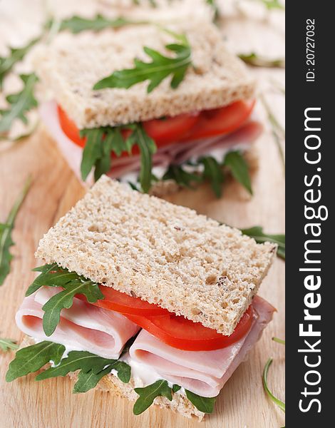 Sandwich with ham,tomato, and rucola salad on the wooden cutting board