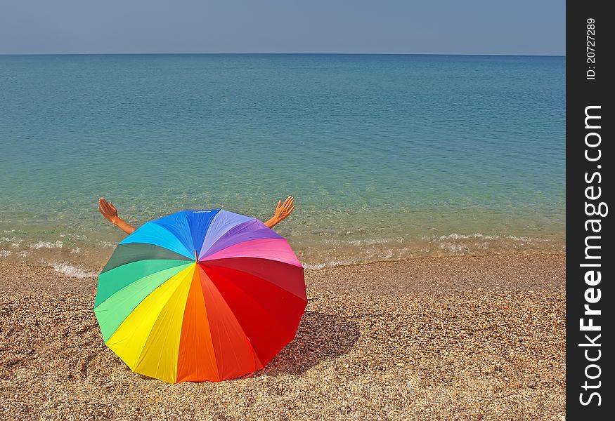 Rainbow colorful beach umbrella, woman hands and sea. Rainbow colorful beach umbrella, woman hands and sea