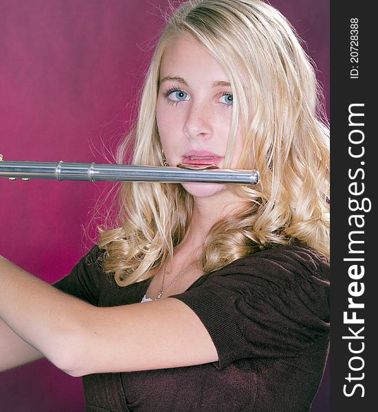 A blond blue eyed teenage female girl holding a silver flute against a pink background. A blond blue eyed teenage female girl holding a silver flute against a pink background.