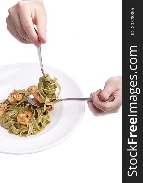 Hand holding fork and spoon for eating tagliatelle with shrimps,herbs and olive oil. tagliatelle swirled around a fork.