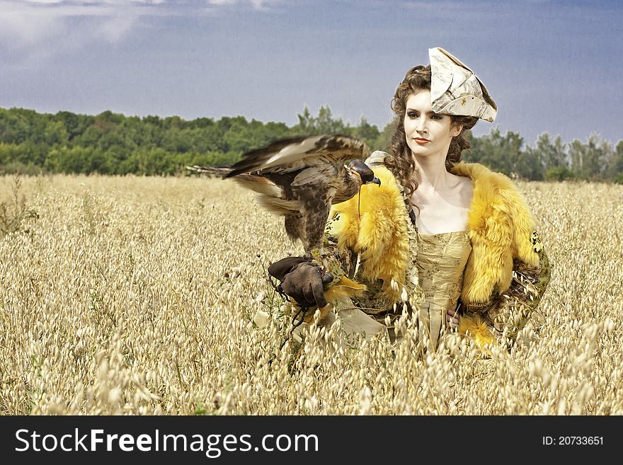 The woman in a beautiful old style dress with falcon has a rest before hunting in yellow field. The woman in a beautiful old style dress with falcon has a rest before hunting in yellow field.