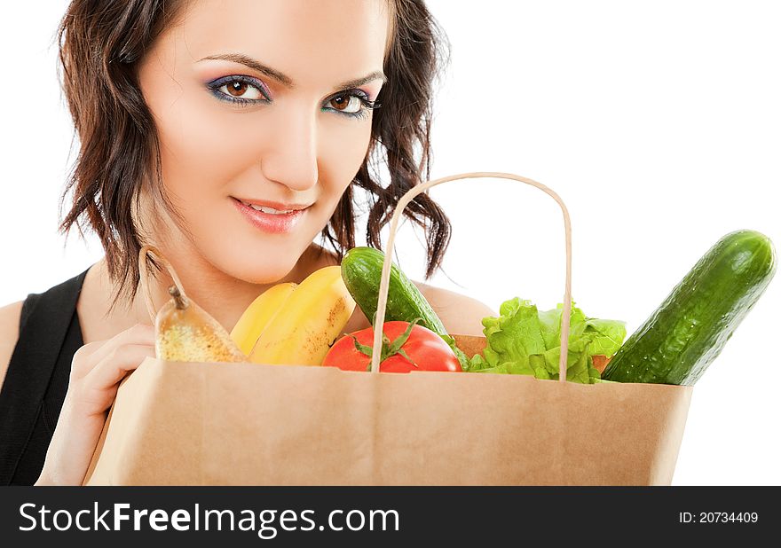 Young female holding paper shopping bag full of groceries, looking at camera. Young female holding paper shopping bag full of groceries, looking at camera