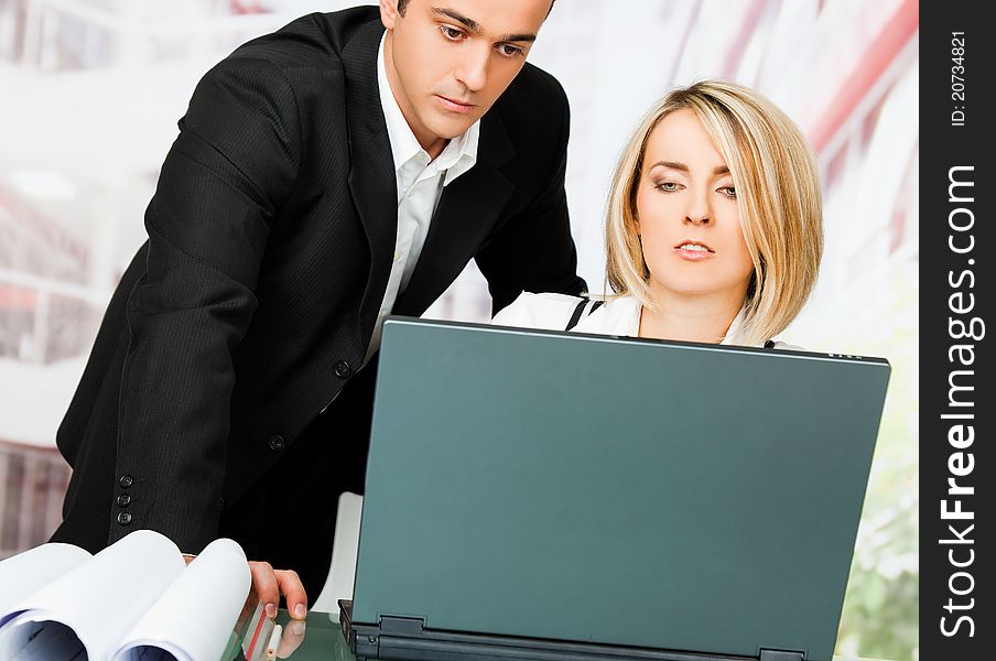 Male and female architects behind laptop and blueprints, looking serious. Male and female architects behind laptop and blueprints, looking serious