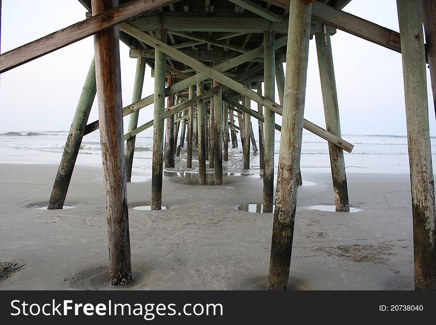 Under Pier, Waves rush through pylons on beach as tide recedes.