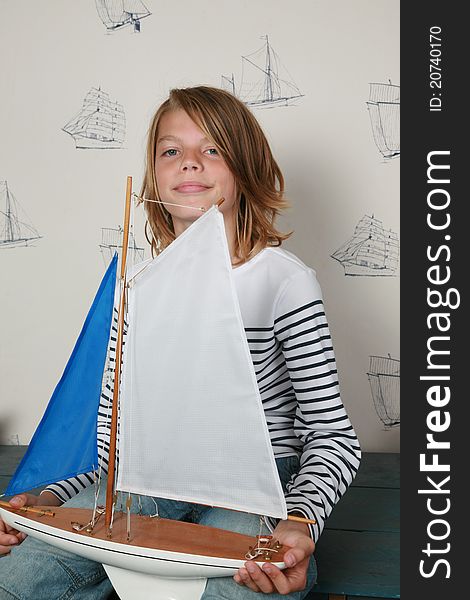 Young boy sitting on table holding toy sailboat on his hands. Young boy sitting on table holding toy sailboat on his hands