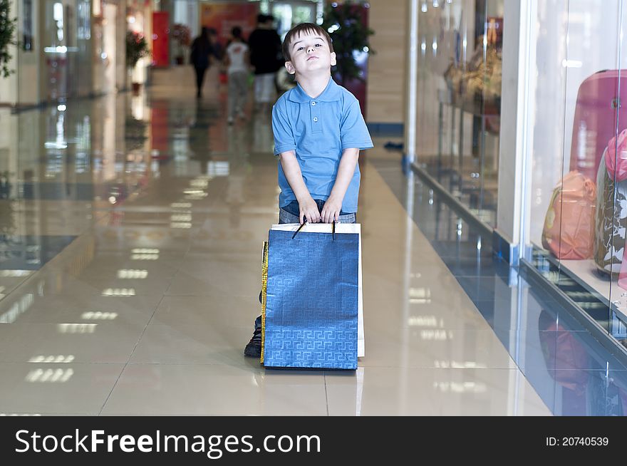 The child bears packages with purchases in shopping center. The child bears packages with purchases in shopping center