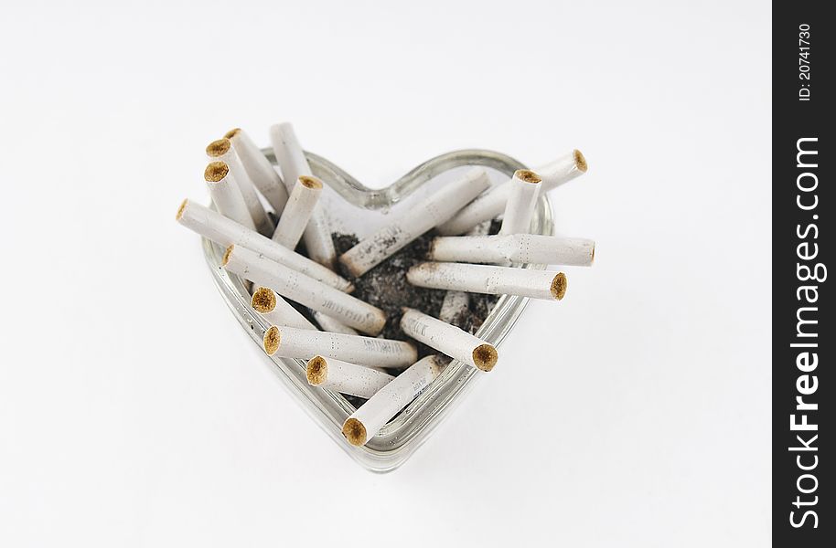 Glass heart with cigarette butts on a white background