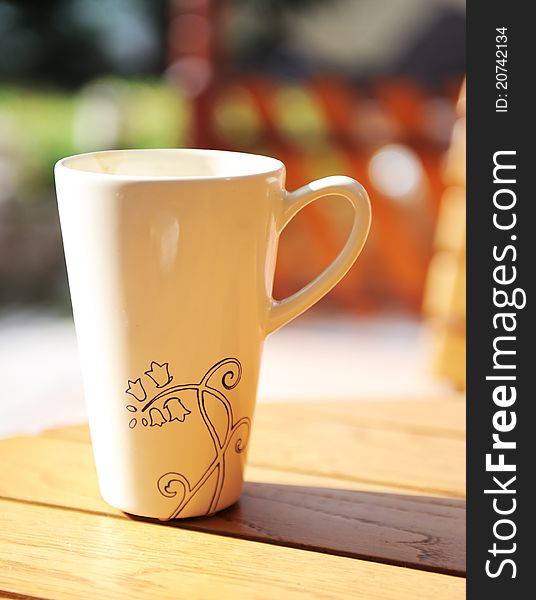 White mug with ornament on table with outdoor setting. White mug with ornament on table with outdoor setting