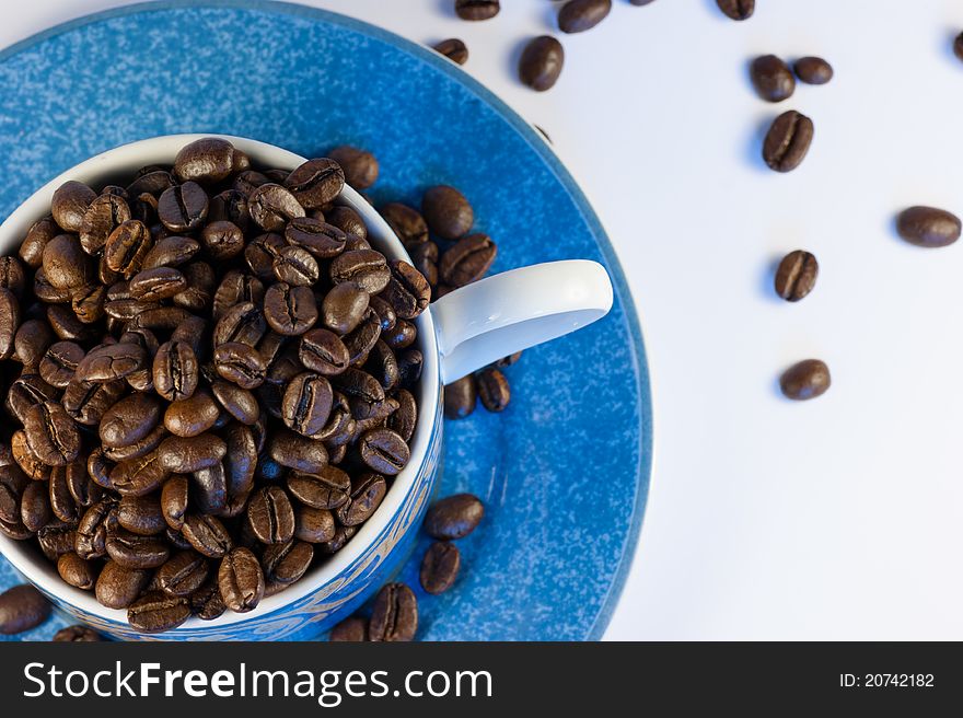 Dark roasted coffee beans in a cup and saucer. Dark roasted coffee beans in a cup and saucer