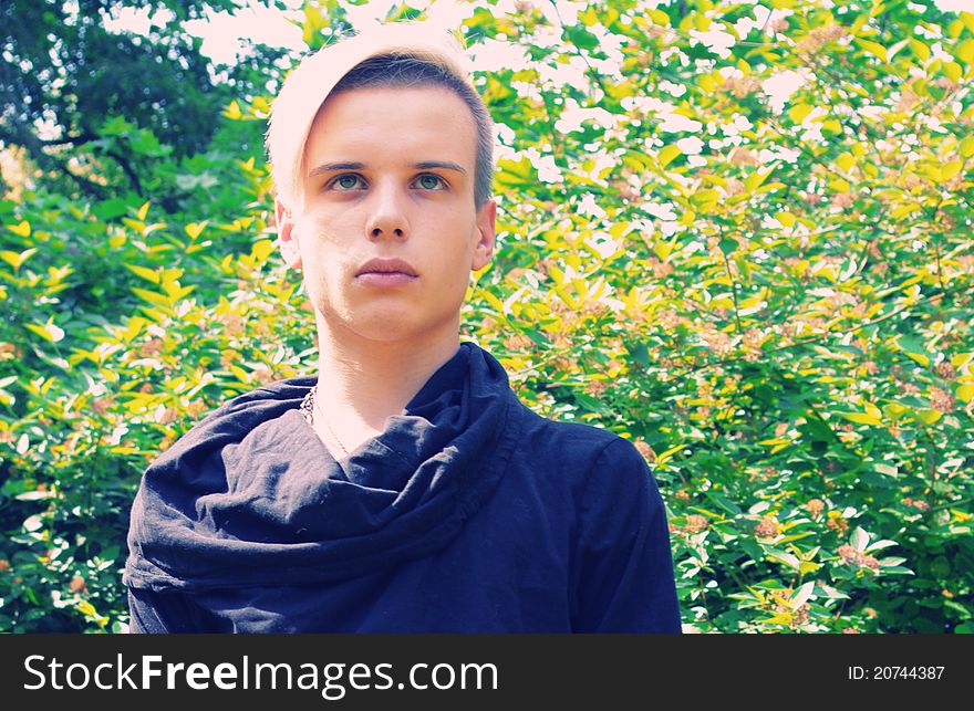 Young man with hairstyle in front of green and yellow leaves