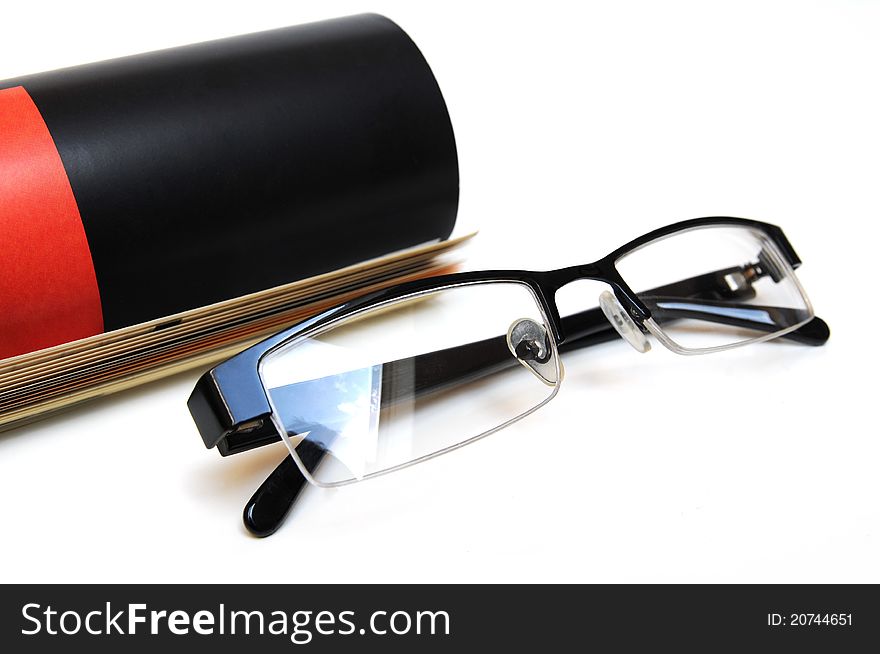 Black and red colored magazine with glasses in front over white background