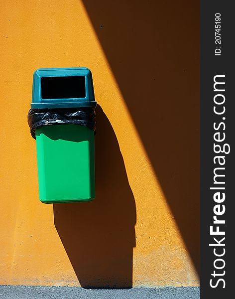 Green bin in the steet, orange wall with strong shadows