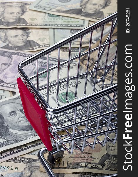 A shopping cart standing on various denominations of American money.