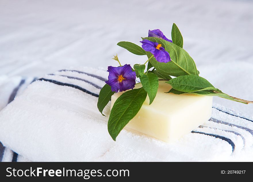 Beautiful violet flowers and soap on rolled up striped white and blue towels stacked on the bed