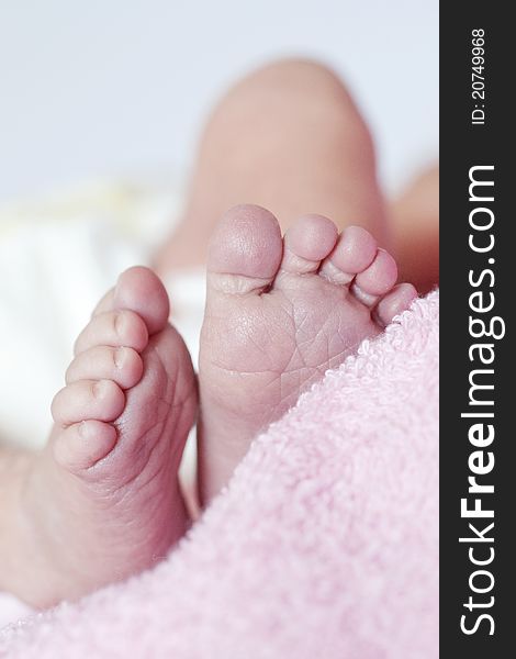 Small feet of a newborn lying on pink towel and white background