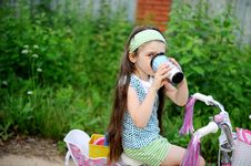 Long-haired Child Girl Drinks While Riding Bike Royalty Free Stock Photography