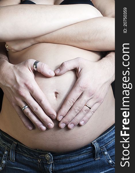 Happy pregnant woman on black background with crossed arms and hands of the father a heart-shaped on the belly. Happy pregnant woman on black background with crossed arms and hands of the father a heart-shaped on the belly