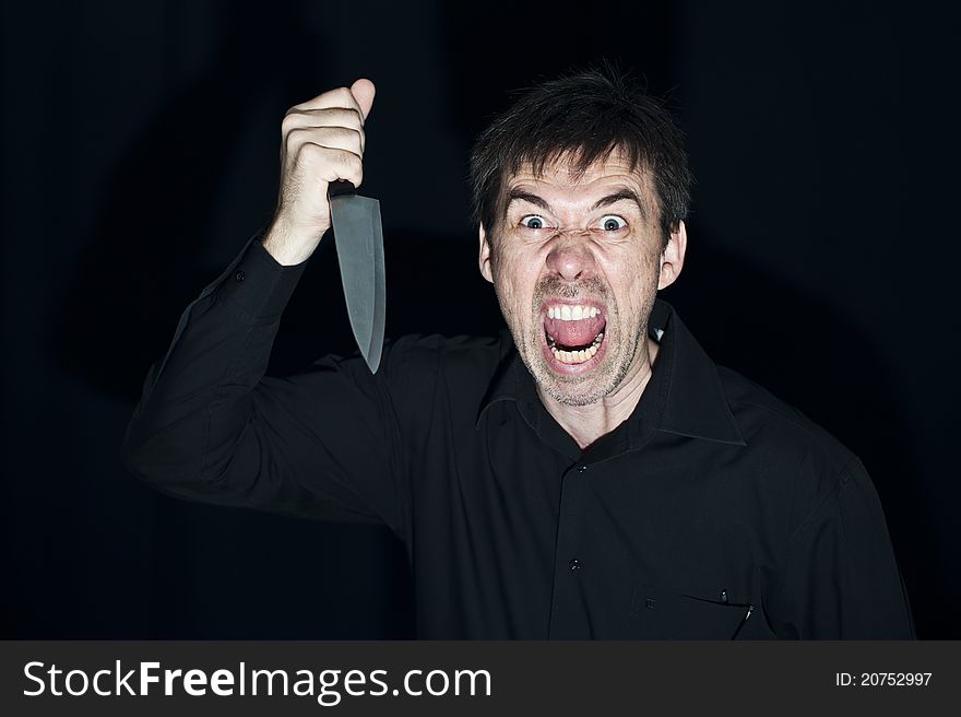 A crazy person with angry expression wielding a knife, on a black background. Low key lighting for dramatic effect. A crazy person with angry expression wielding a knife, on a black background. Low key lighting for dramatic effect.