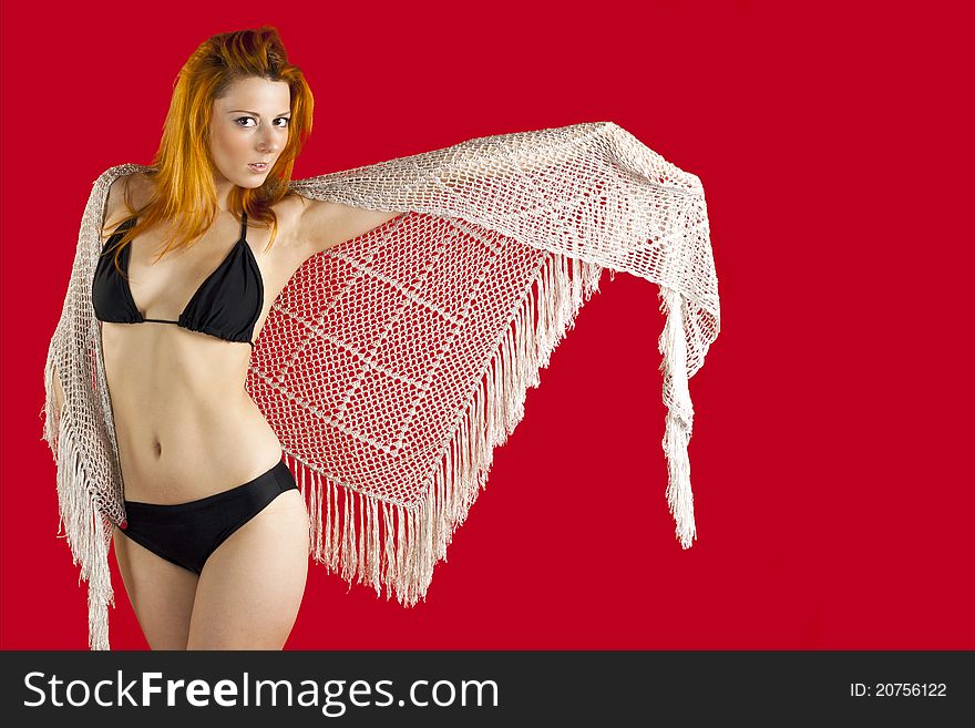 Red-haired young woman in a black bikini, with knitted scarf and a red background