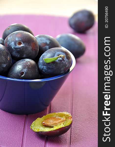 Fresh ripe plums in a navy blue bowl on purple background