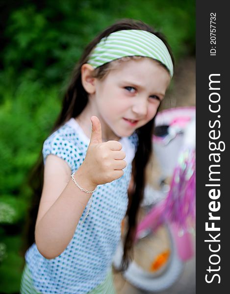 Beautiful long-haired child girl poses outdoors with thumbs up, focus on hand. Beautiful long-haired child girl poses outdoors with thumbs up, focus on hand