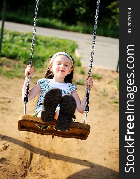 Happy child girl wearing green headband swings in the park. Happy child girl wearing green headband swings in the park