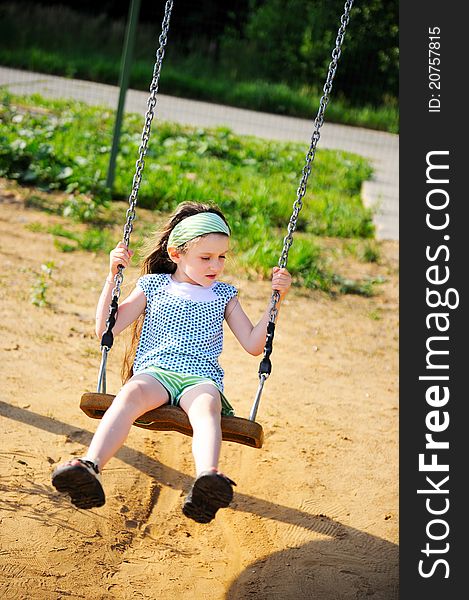 Happy child girl is swinging in the playground