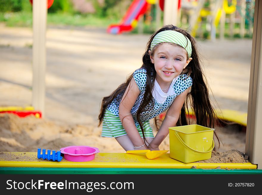 Happy child girl wearing green headband plays in a sandbox. Happy child girl wearing green headband plays in a sandbox