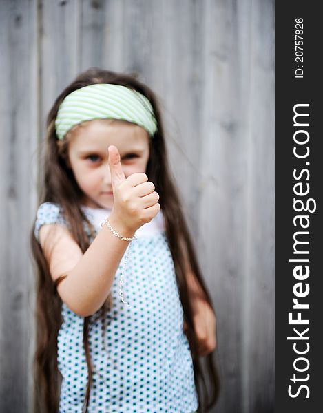 Beautiful long-haired child girl poses outdoors with thumbs up, focus on hand. Beautiful long-haired child girl poses outdoors with thumbs up, focus on hand