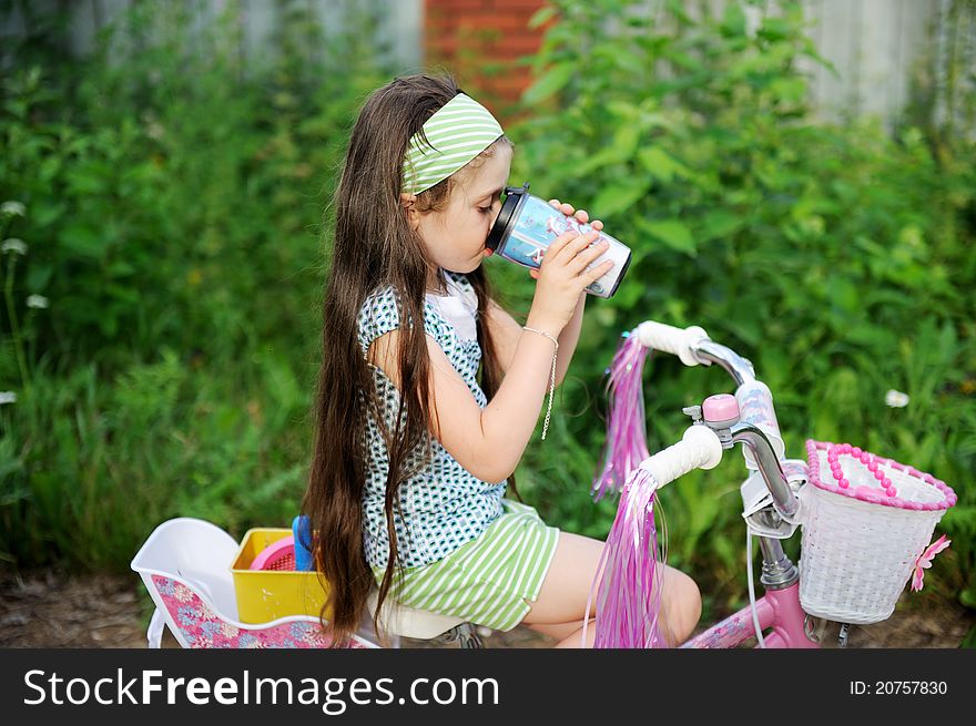 Adorable brunette child girl drinks while riding her pink bike. Adorable brunette child girl drinks while riding her pink bike