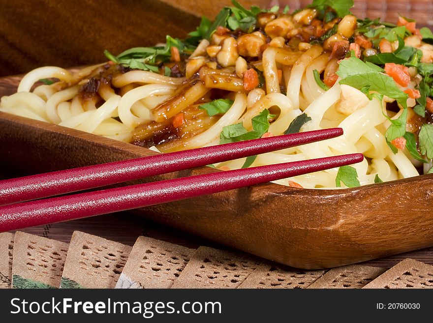 Close-up photograph of red chopsticks on a plate of freshly prepared Asian noodles.