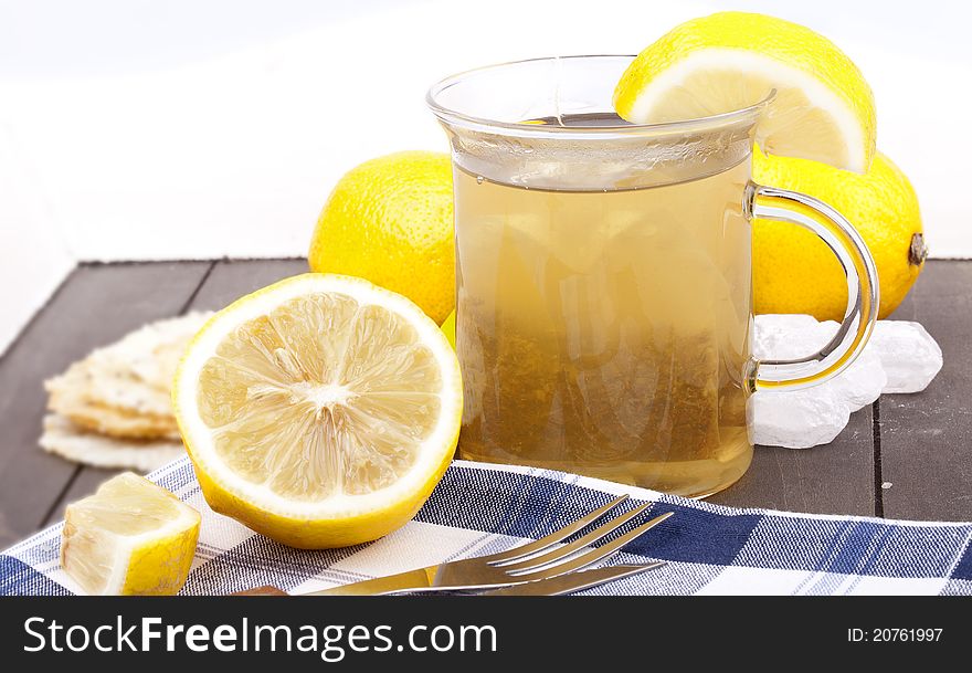 Studio-shot of a glass with hot lemon tea, a slice of lemon and rock sugar, on a wooden tray.