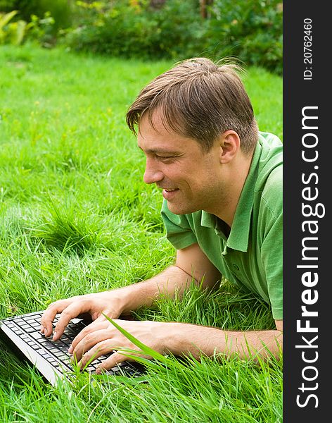 Cute man with laptop lies on grass