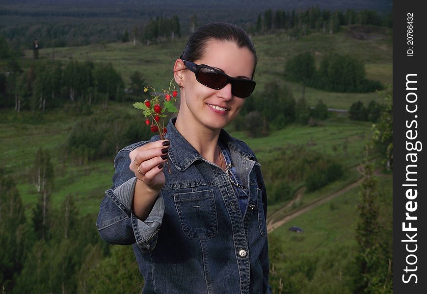 The beautiful smiling young woman holds in a hand a branch with wild strawberry berries. The beautiful smiling young woman holds in a hand a branch with wild strawberry berries