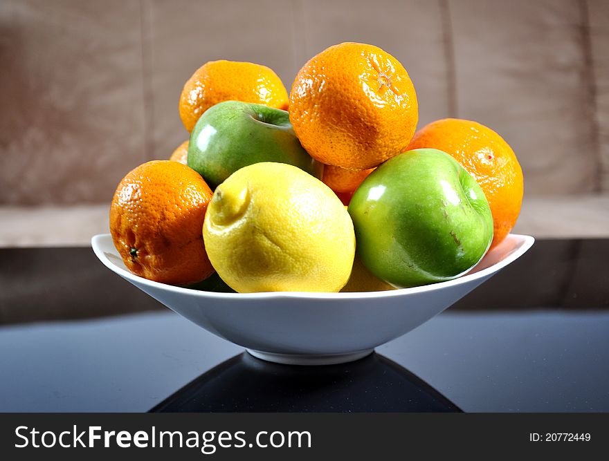 Mandarins, oranges, apples and lemons in a ceramic bowl, on a home background. Mandarins, oranges, apples and lemons in a ceramic bowl, on a home background