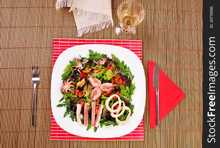 Italian fish salad on table with white wine glass, knife and fork