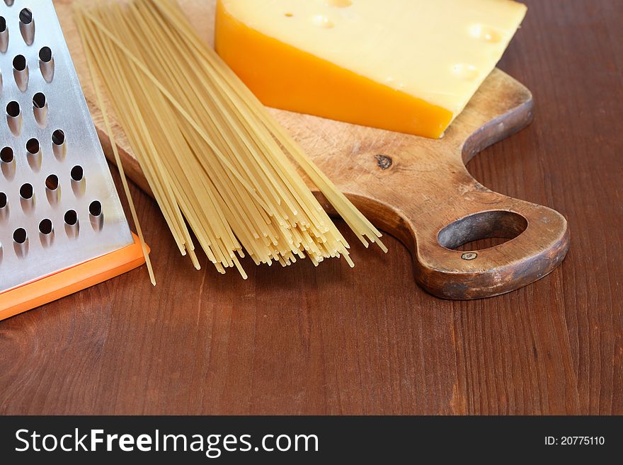 Raw spaghetti near grater and cheese on wooden surface. Raw spaghetti near grater and cheese on wooden surface