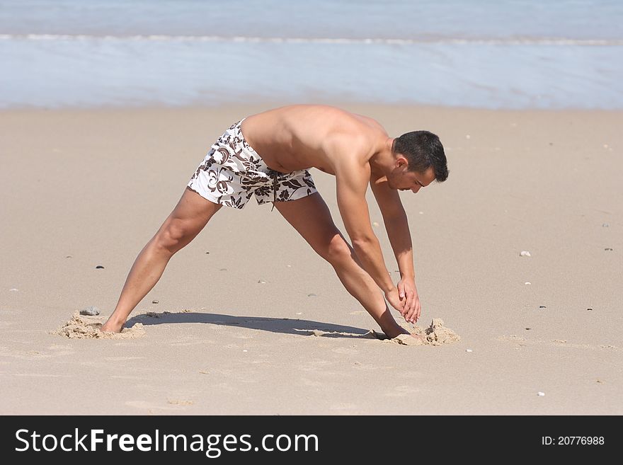 Attractive man making stretching movements before run on the beach