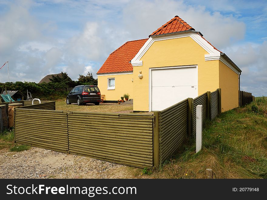 There are a modern house, a garage and a car in the yard against the sky. The yard is enclosed with fence. There are a modern house, a garage and a car in the yard against the sky. The yard is enclosed with fence.