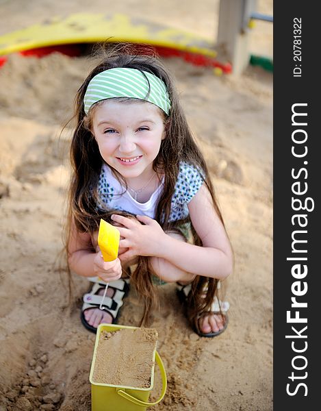 Happy child girl wearing green headband plays in a sandbox. Happy child girl wearing green headband plays in a sandbox