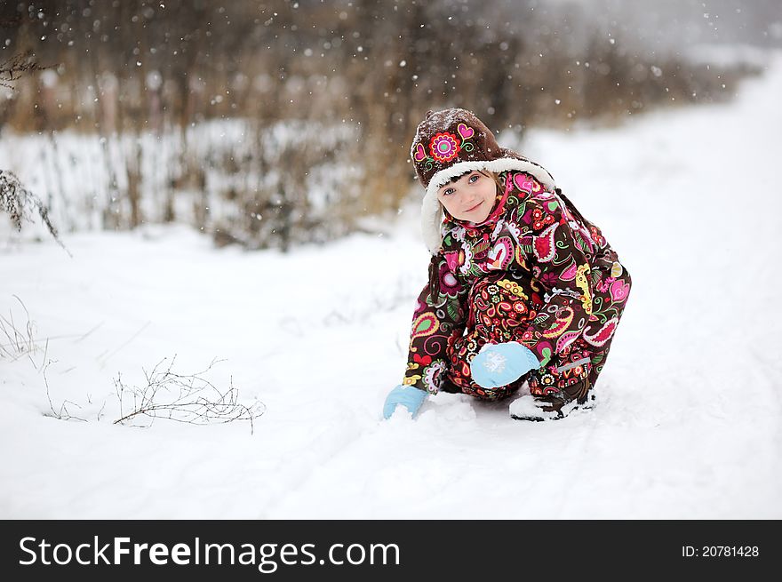 Child girl in colorful snowsiut plays in snow