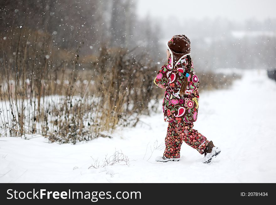 Child girl in colorful snowsiut plays in snow