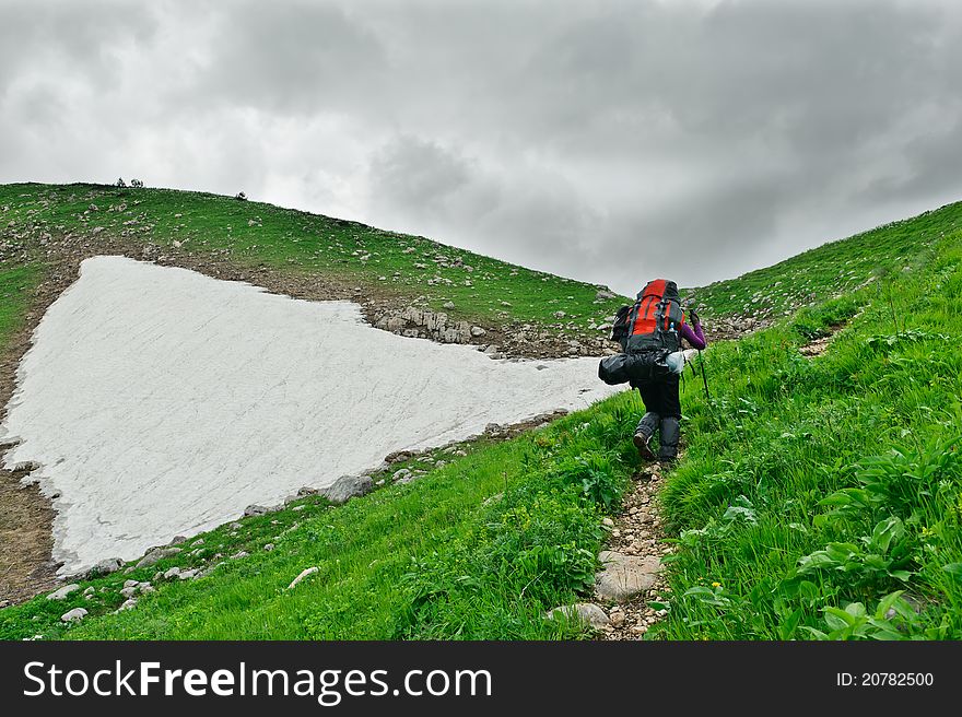 Tourist with a backpack walking along the road in the mountains. The mountains of North Caucasus.