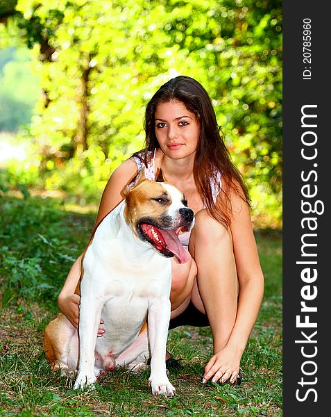 A vary beautiful girl hugging an American Staffordshire Terrier dog outside in a park meadow. A vary beautiful girl hugging an American Staffordshire Terrier dog outside in a park meadow