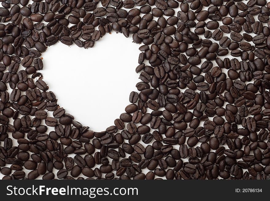 Whole espresso coffee beans spread out on a white surface with a heart-shaped hole. Whole espresso coffee beans spread out on a white surface with a heart-shaped hole.
