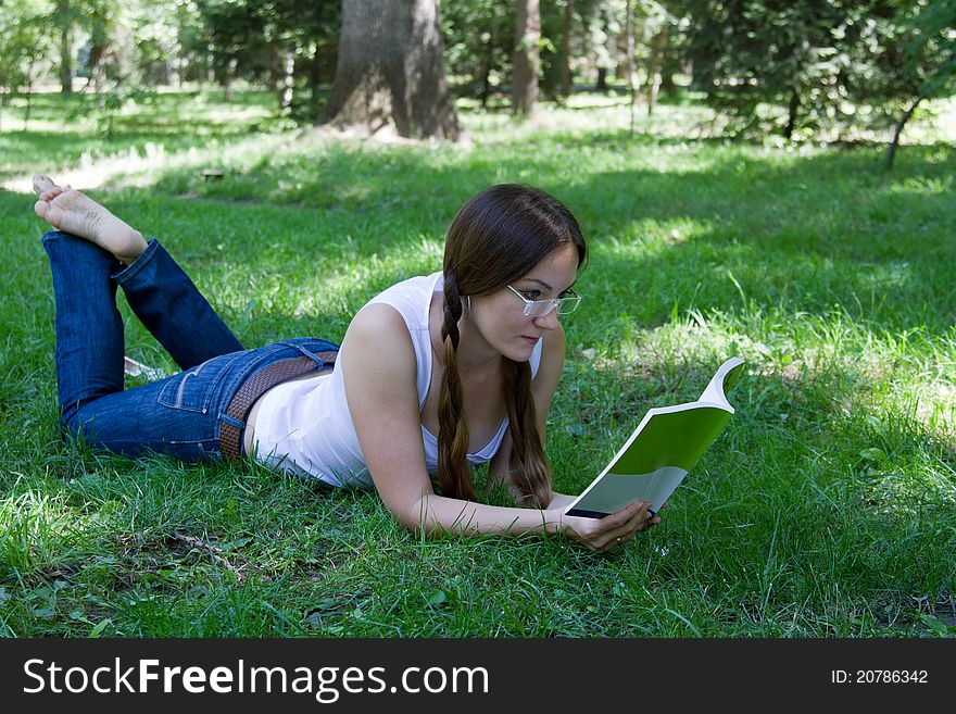 Beautiful woman with two braids wearing jeans lying on the grass with a book in the park. Beautiful woman with two braids wearing jeans lying on the grass with a book in the park