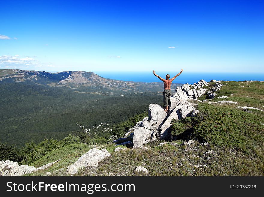 Sports man bared on a belt, costs on a rock in mountains, having lifted upwards hands, on a back background the sea and the blue sky with clouds. Sports man bared on a belt, costs on a rock in mountains, having lifted upwards hands, on a back background the sea and the blue sky with clouds