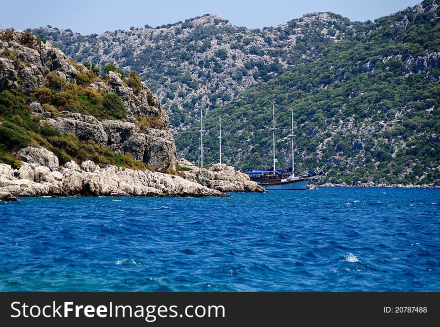 The yacht in harbor among rocks and blue sea.